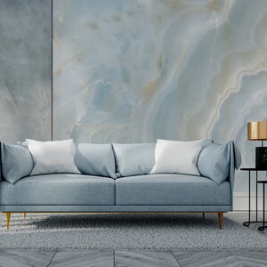 May include: A light blue sofa with white pillows sits in front of a wall with a blue and white marble pattern. Two black side tables with gold lamps are on either side of the sofa. A gray rug is on the floor.