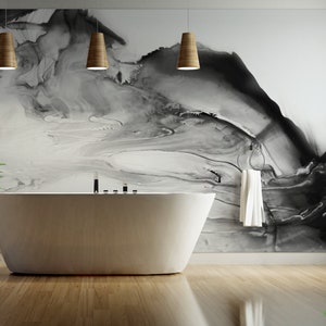 May include: A white bathtub sits in a modern bathroom with a black and white abstract art print on the wall. Three wooden pendant lights hang above the tub.