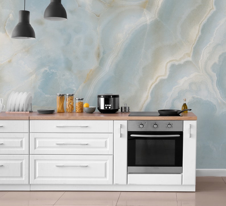 May include: White kitchen cabinets with a stainless steel oven and a black countertop. The backsplash is a light blue and white marble pattern.