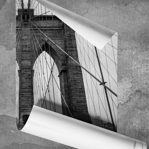 May include: A black and white photograph of the Brooklyn Bridge in New York City. The image is cropped to show the bridge's towers and cables.