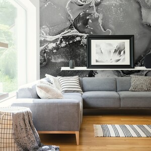 May include: A grey sectional sofa with cushions and a throw blanket sits in a living room with a black and white abstract wall mural, a black framed picture, and a black and white striped rug.