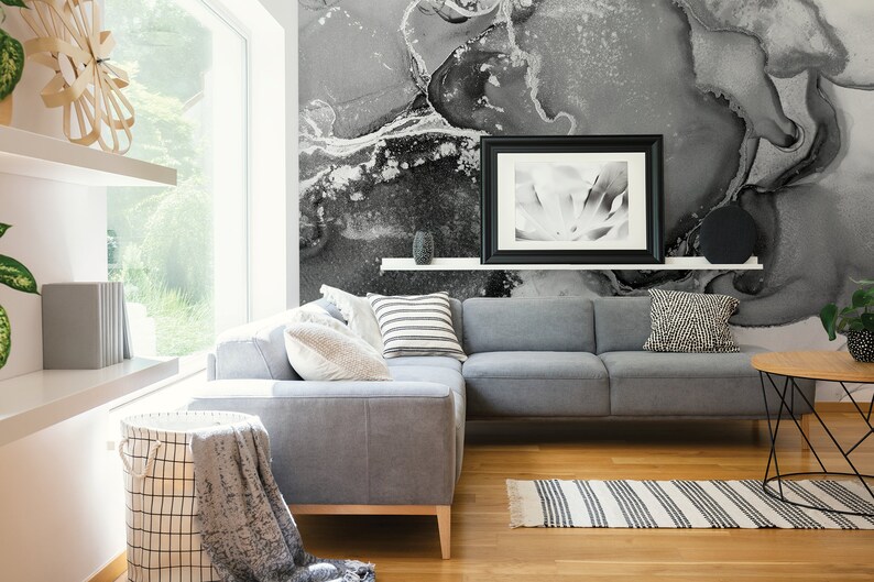 May include: A grey sectional sofa with cushions and a throw blanket sits in a living room with a black and white abstract wall mural, a black framed picture, and a black and white striped rug.
