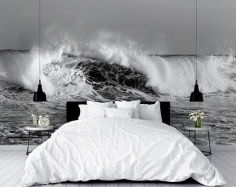Puede incluir: Una cama blanca con ropa de cama blanca y una cabecera negra se encuentra frente a un mural fotográfico en blanco y negro de una gran ola rompiendo en el océano.