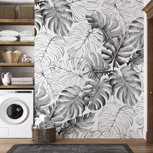 May include: A white washing machine with a black and white tropical leaf wallpaper behind it. The wallpaper features large, stylized leaves in a watercolor style.