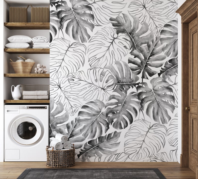 May include: A white washing machine with a black and white tropical leaf wallpaper behind it. The wallpaper features large, stylized leaves in a watercolor style.