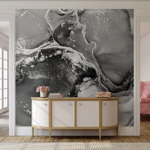 May include: A white cabinet with gold trim and four doors sits in front of a wall with a black and white abstract marble pattern wallpaper.
