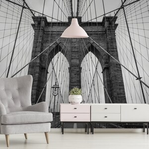 May include: A black and white photograph of the Brooklyn Bridge in New York City. The bridge is a suspension bridge with two towers and a roadway that connects Brooklyn and Manhattan. The photo is taken from below the bridge, looking up at the towers and the cables.