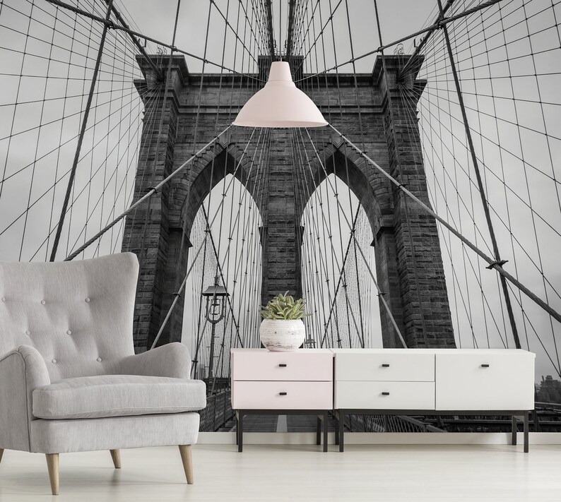 May include: A black and white photograph of the Brooklyn Bridge in New York City. The bridge is a suspension bridge with two towers and a roadway that connects Brooklyn and Manhattan. The photo is taken from below the bridge, looking up at the towers and the cables.