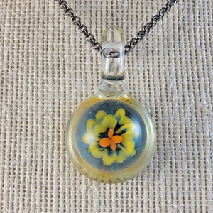 May include: A glass pendant necklace with a silver chain. The pendant is a clear glass sphere with a yellow and orange flower inside.