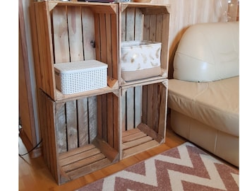 Könnte beinhalten: Ein Holzregal aus recycelten Kisten. Das Regal besteht aus vier gestapelten Kisten mit Pflanzen, einem weißen Korb und einer kleinen Box oben. Ein gemusterter Teppich und ein beiges Sofa sind im Hintergrund zu sehen.
