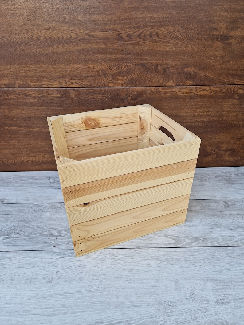 May include: A natural wood crate with a rectangular shape and a handle on the side. The crate is made of unfinished wood and has a rustic look.