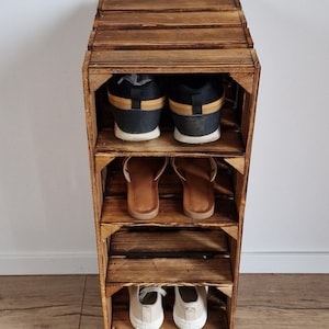 May include: A rustic, wooden shoe rack with multiple shelves, holding various pairs of shoes. The rack is made of stained wood, showcasing the natural grain. Shoes include sneakers, sandals, and flats, offering a glimpse of the rack's storage capacity.