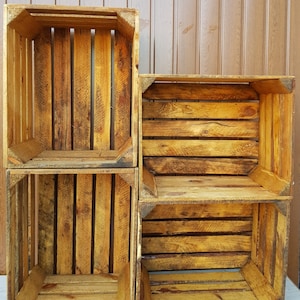 May include: Four wooden crates stacked together. The crates are made of weathered wood with a warm, golden-brown hue. The design features vertical and horizontal wooden slats, creating an open, box-like structure. The crates appear to be vintage or rustic.