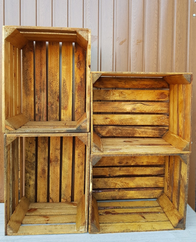 May include: Four wooden crates stacked together. The crates are made of weathered wood with a warm, golden-brown hue. The design features vertical and horizontal wooden slats, creating an open, box-like structure. The crates appear to be vintage or rustic.