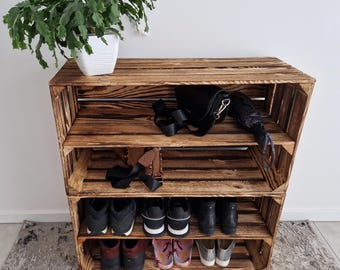 Könnte beinhalten: Ein rustikales Schuhregal aus recycelten Holzkisten. Das Regal hat drei Regale mit Schuhen, einer Handtasche und einem Regenschirm. Oben steht eine Topfpflanze. Das Holz hat eine warme, braune Oberfläche.
