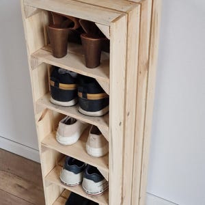 Puede incluir: Un zapatero vertical alto construido con listones de madera clara sin tratar. La unidad cuenta con seis estantes abiertos, cada uno con un par de zapatos, incluyendo sandalias de tac&oacute;n marr&oacute;n, zapatillas negras, zapatillas blancas y zapatos.