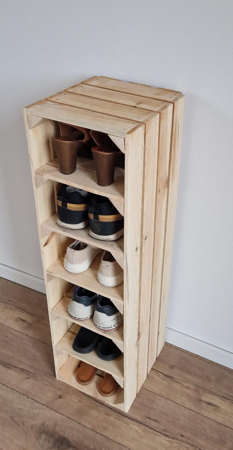 Puede incluir: Un zapatero vertical alto construido con listones de madera clara sin tratar. La unidad cuenta con seis estantes abiertos, cada uno con un par de zapatos, incluyendo sandalias de tac&oacute;n marr&oacute;n, zapatillas negras, zapatillas blancas y zapatos.