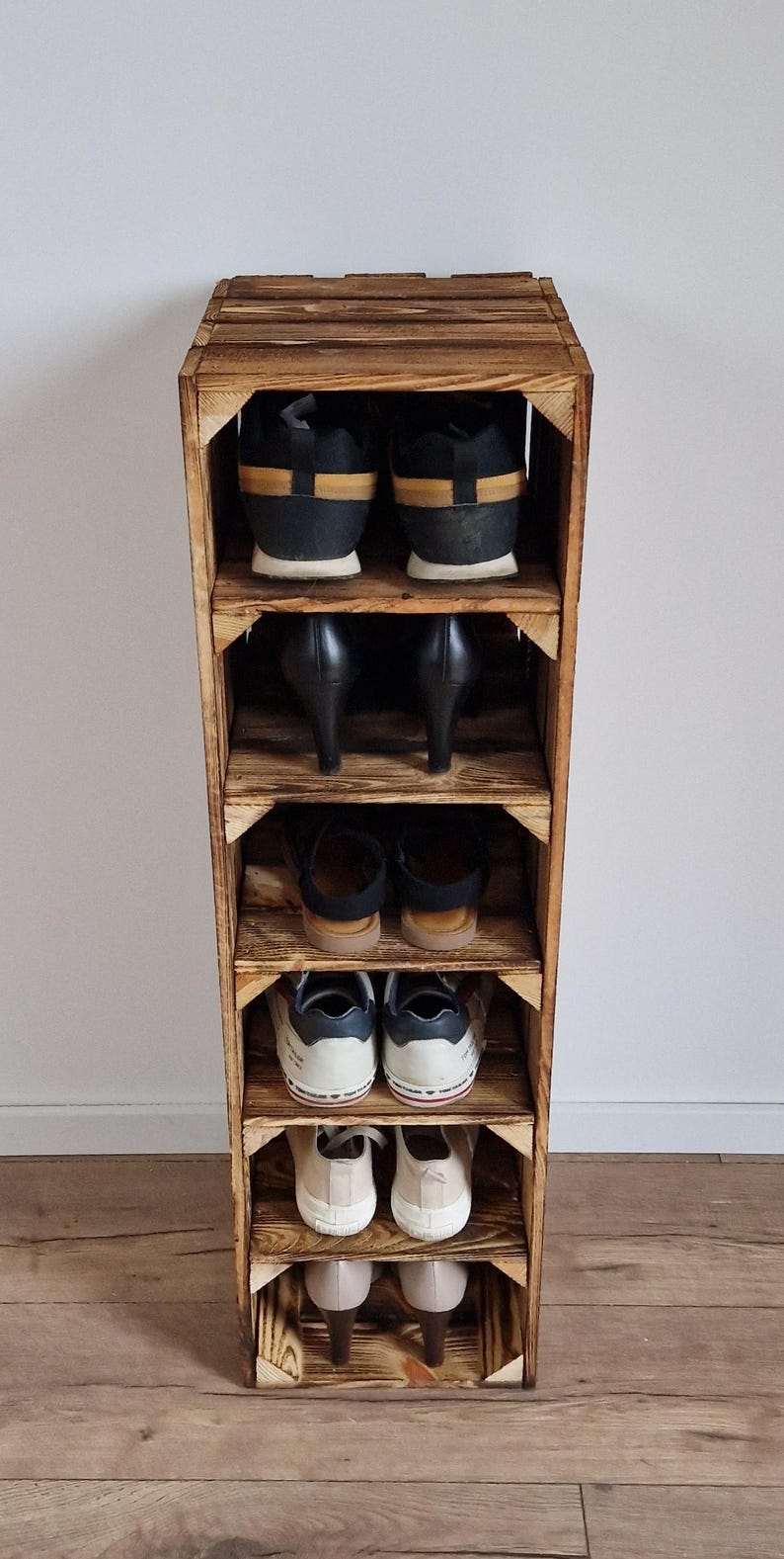 May include: A rustic, wooden shoe rack with multiple shelves, showcasing various pairs of shoes. The rack is made of light brown wood and has a simple, functional design. The shoes include sneakers, heels, and flats, offering a glimpse of different footwear styles.