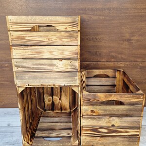 May include: Three wooden crates stacked on top of each other. The crates are made of natural wood with a rustic, weathered look. The crates are empty and have a rectangular shape.