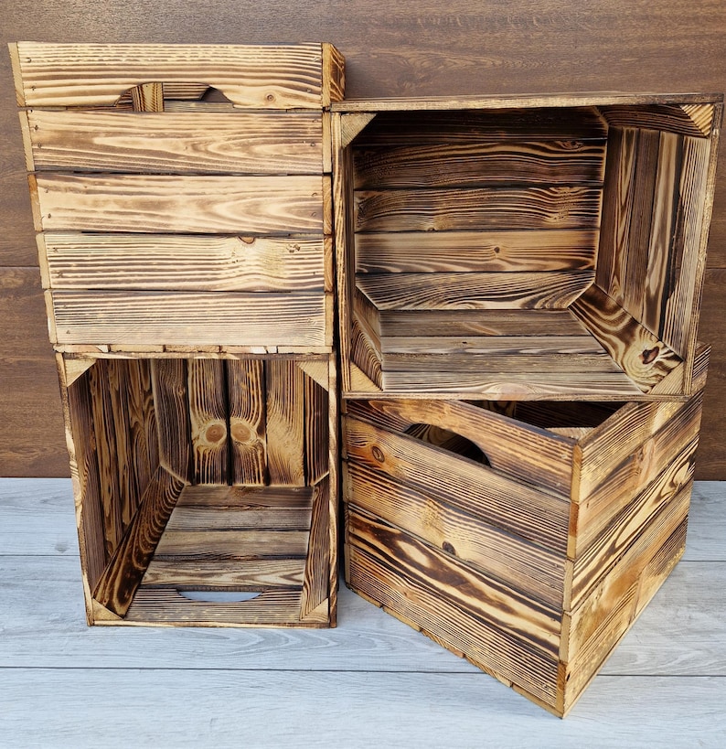 May include: Four rustic wooden crates stacked on top of each other. The crates are made of natural wood with a dark brown finish. Each crate has a rectangular shape with a handle on the side.