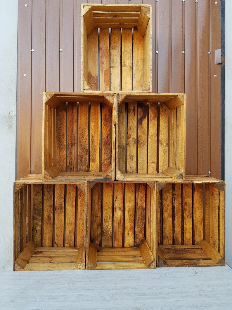 May include: A stack of five rectangular wooden crates arranged in a pyramid formation. Each crate is constructed from light brown, unfinished wood slats with visible grain patterns and open fronts, creating a modular storage display.