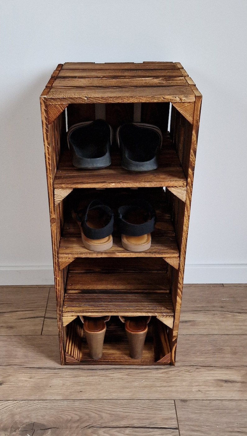 May include: A rustic, wooden shoe rack with three shelves. The rack is made from reclaimed wood, with a dark brown finish. The shelves hold various pairs of shoes, including sandals and heels. The rack is designed to be a space-saving storage solution.