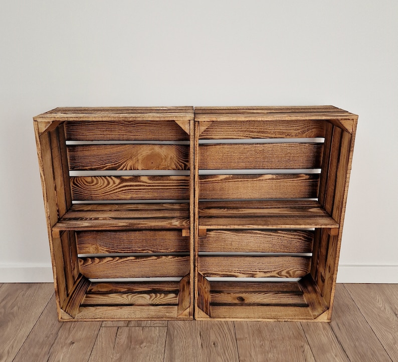 May include: Two rustic wooden crates, stained in a warm brown hue, are positioned side-by-side. Each crate features a slatted design with interior shelves, offering storage or display space. The wood grain is visible, adding to the natural aesthetic.