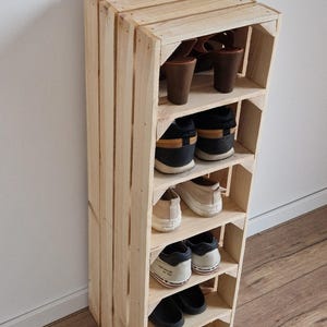 Puede incluir: Un zapatero vertical alto construido con listones de madera clara sin tratar. La unidad cuenta con seis estantes horizontales, cada uno con un par de zapatos, incluyendo sandalias de tac&oacute;n marrones, zapatillas deportivas y sandalias planas.