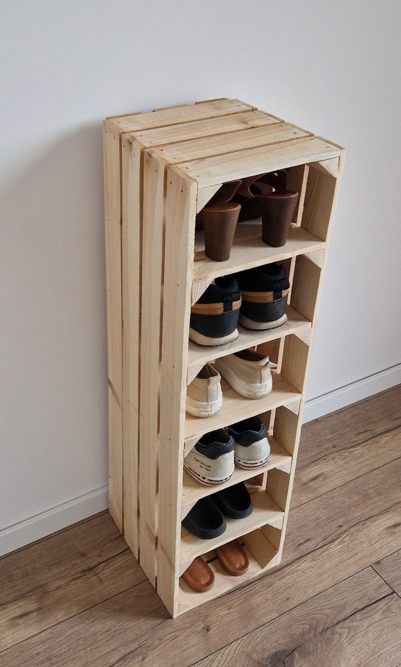 Puede incluir: Un zapatero vertical alto construido con listones de madera clara sin tratar. La unidad cuenta con seis estantes horizontales, cada uno con un par de zapatos, incluyendo sandalias de tac&oacute;n marrones, zapatillas deportivas y sandalias planas.