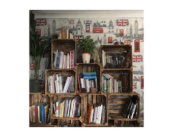 Könnte beinhalten: Ein rustikales Bücherregal aus Holzkisten, gefüllt mit Büchern verschiedener Größen und Farben. Die Kisten sind in einer gestapelten Konfiguration vor einer Tapete mit Londoner Wahrzeichen und Union Jack-Flaggen angeordnet. Eine Topfpflanze ist sichtbar.