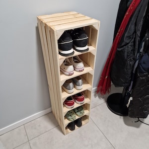 May include: A wooden shoe rack with multiple shelves, holding various pairs of shoes. The rack is made from light-colored wood and has a rustic, handmade appearance. The shoes include sneakers, flats, and other casual footwear.
