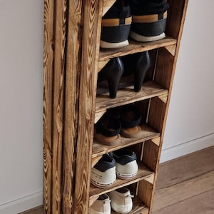 Puede incluir: Un zapatero vertical alto construido con cajas de madera te&ntilde;idas de oscuro con patrones de veta visibles. La unidad cuenta con cinco estantes horizontales, cada uno con un par de zapatos, incluyendo zapatillas, tacones y calzado plano.