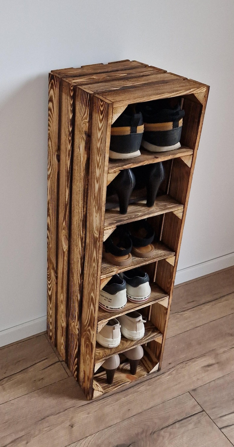 Puede incluir: Un zapatero vertical alto construido con cajas de madera te&ntilde;idas de oscuro con patrones de veta visibles. La unidad cuenta con cinco estantes horizontales, cada uno con un par de zapatos, incluyendo zapatillas, tacones y calzado plano.