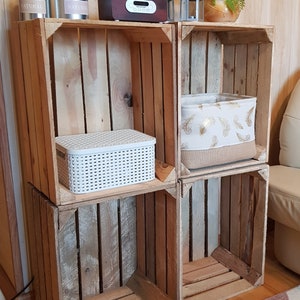 May include: A set of four wooden crates stacked on top of each other to create a shelf unit. The crates are made of natural wood and have a rustic look. The shelves are decorated with plants, a radio, candles, and storage baskets.
