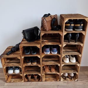 Puede incluir: Una unidad de almacenamiento escalonada construida con cuatro cajas de madera te&ntilde;ida oscura de diferentes alturas. La unidad cuenta con m&uacute;ltiples estantes abiertos que contienen varios pares de zapatos, incluyendo zapatillas, sandalias y tacones, junto con dos bolsos y un paraguas.