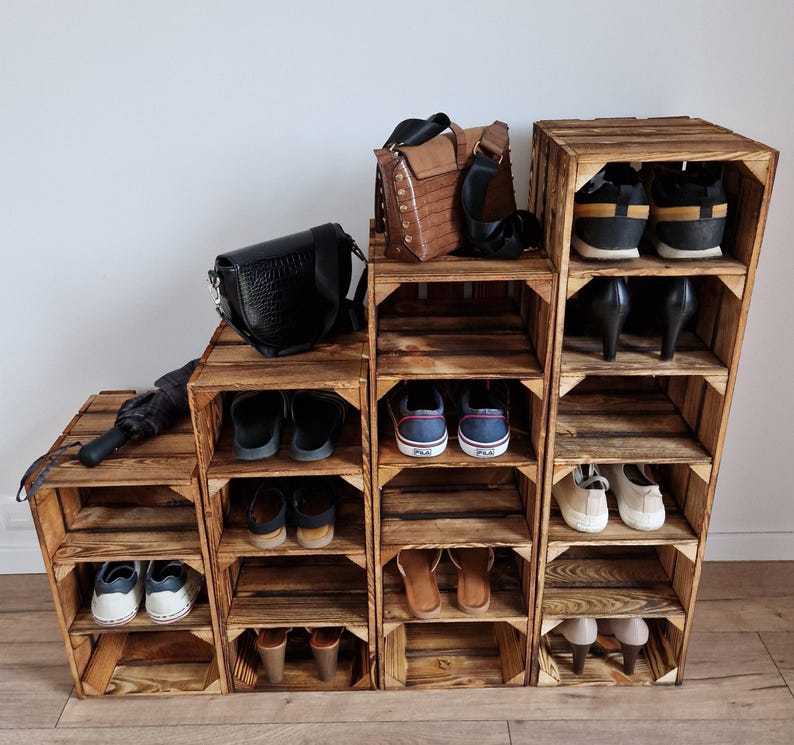 Puede incluir: Una unidad de almacenamiento escalonada construida con cuatro cajas de madera te&ntilde;ida oscura de diferentes alturas. La unidad cuenta con m&uacute;ltiples estantes abiertos que contienen varios pares de zapatos, incluyendo zapatillas, sandalias y tacones, junto con dos bolsos y un paraguas.