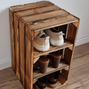 May include: A rustic, three-tiered wooden shoe rack. The rack is constructed from stained wood, showcasing visible grain. It holds various pairs of shoes, including sneakers and sandals. The design is simple and functional, suitable for home organization.