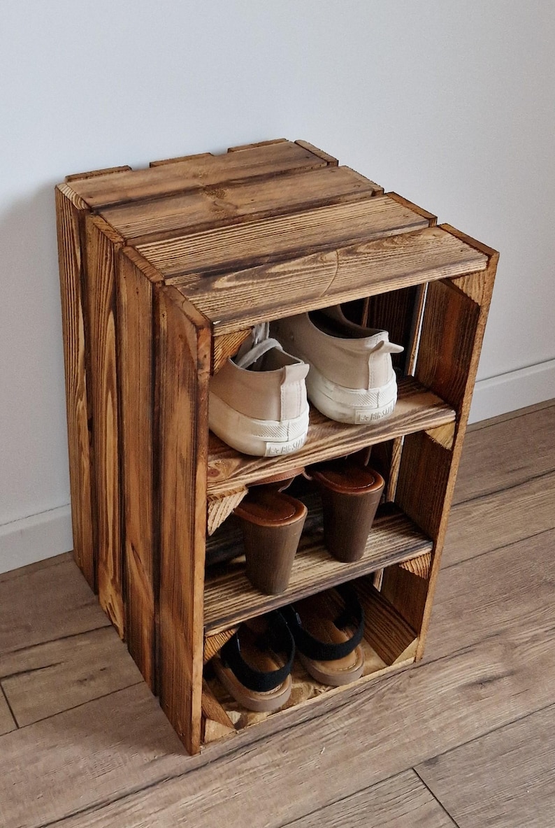 May include: A rustic, three-tiered wooden shoe rack. The rack is constructed from stained wood, showcasing visible grain. It holds various pairs of shoes, including sneakers and sandals. The design is simple and functional, suitable for home organization.