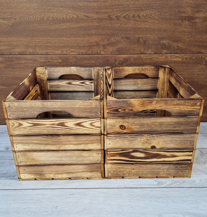 May include: Two wooden crates with a rustic, burnt finish. The crates are stacked on top of each other and have a handle on each side.