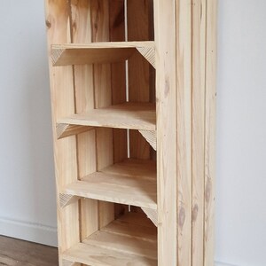 May include: A tall, unfinished wooden shelf unit with five shelves. The shelves are supported by triangular corner pieces. The unit is made of light-colored wood and has a simple, rustic design. The unit is approximately 48 inches tall.
