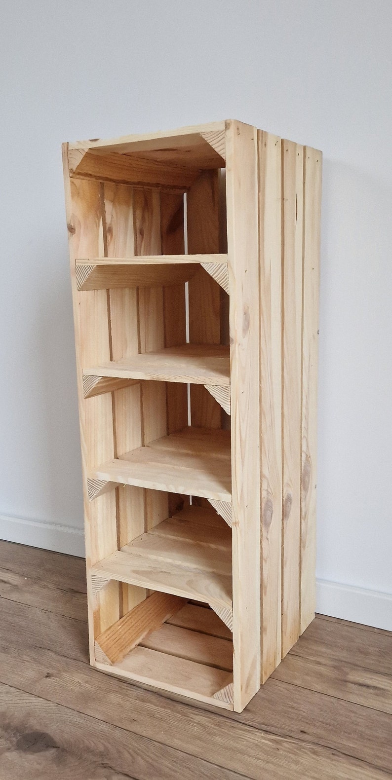 May include: A tall, unfinished wooden shelf unit with five shelves. The shelves are supported by triangular corner pieces. The unit is made of light-colored wood and has a simple, rustic design. The unit is approximately 48 inches tall.