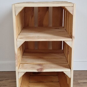 May include: A three-tiered wooden crate shelf made of light-colored wood. The shelf has three open compartments and is constructed with visible wood grain and corner supports. The crate is designed for storage or display.