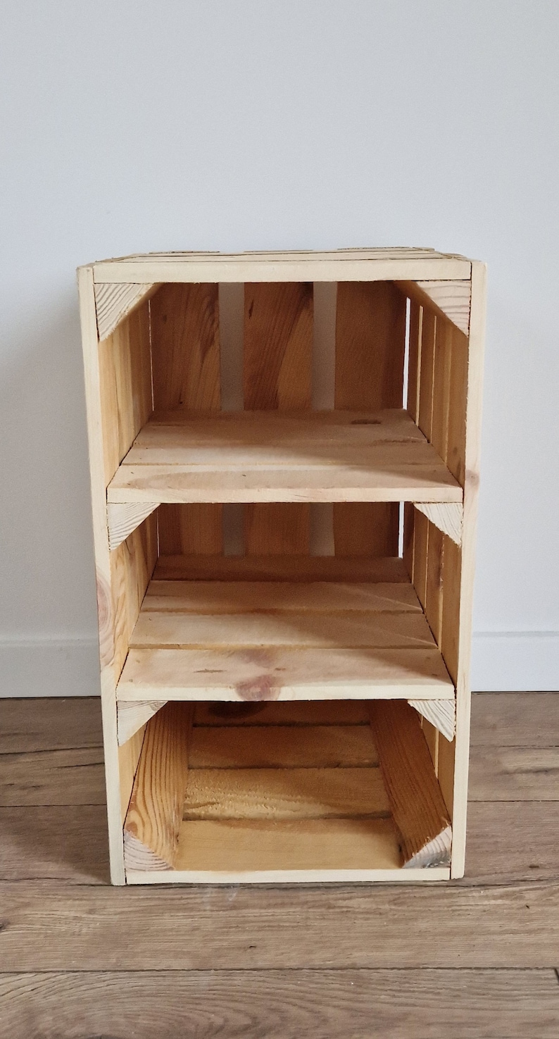 May include: A three-tiered wooden crate shelf made of light-colored wood. The shelf has three open compartments and is constructed with visible wood grain and corner supports. The crate is designed for storage or display.
