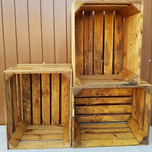 May include: Three rustic wooden crates, stacked and arranged. The crates are constructed from weathered, light brown planks, showcasing visible wood grain and knots. The open design of the crates suggests they are suitable for storage or display purposes.