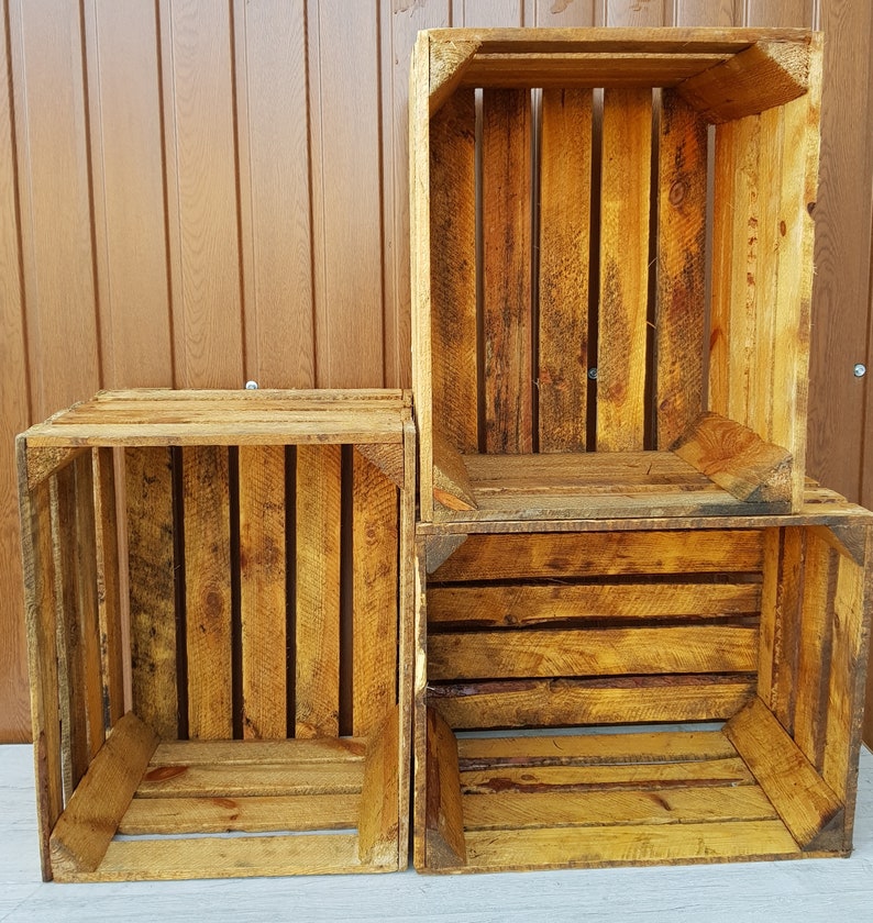 May include: Three rustic wooden crates, stacked and arranged. The crates are constructed from weathered, light brown planks, showcasing visible wood grain and knots. The open design of the crates suggests they are suitable for storage or display purposes.