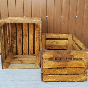 May include: Two rustic wooden crates with a weathered appearance. The crates are constructed from wooden planks and have a rectangular shape. The wood has a warm, golden-brown hue, with visible grain and knots.