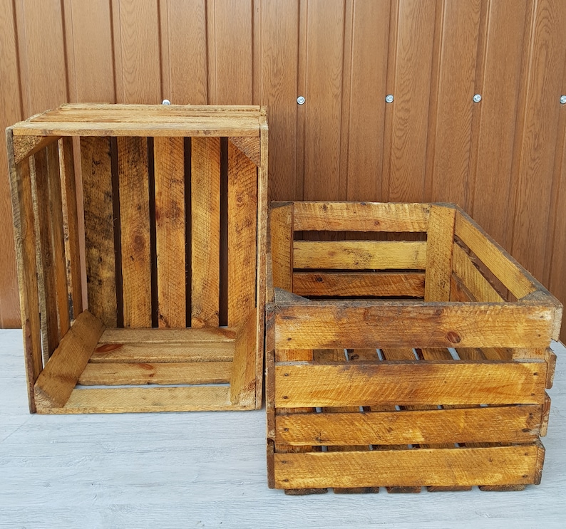May include: Two rustic wooden crates with a weathered appearance. The crates are constructed from wooden planks and have a rectangular shape. The wood has a warm, golden-brown hue, with visible grain and knots.