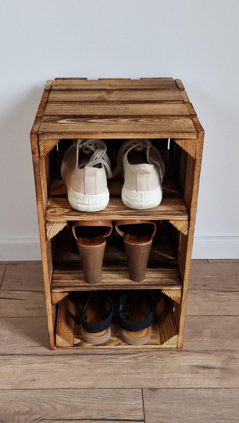 Puede incluir: Una unidad de almacenamiento de tres niveles construida con cajas de madera te&ntilde;idas de oscuro. El estante superior contiene un par de zapatillas beige, el estante central sandalias de cu&ntilde;a marrones y el inferior sandalias negras con tiras.
