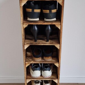 Puede incluir: Un zapatero vertical de madera construido con paneles te&ntilde;idos estilo caja con seis estantes abiertos. Cada estante contiene un par de zapatos, incluyendo zapatillas, tacones y sandalias, dispuestos en filas de arriba a abajo en el marco.