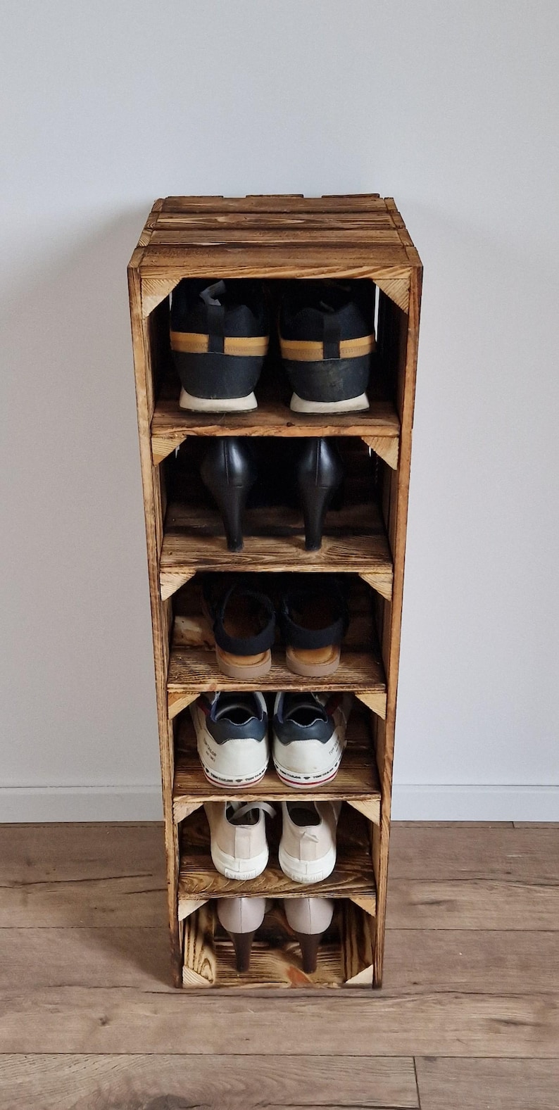 Puede incluir: Un zapatero vertical de madera construido con paneles te&ntilde;idos estilo caja con seis estantes abiertos. Cada estante contiene un par de zapatos, incluyendo zapatillas, tacones y sandalias, dispuestos en filas de arriba a abajo en el marco.